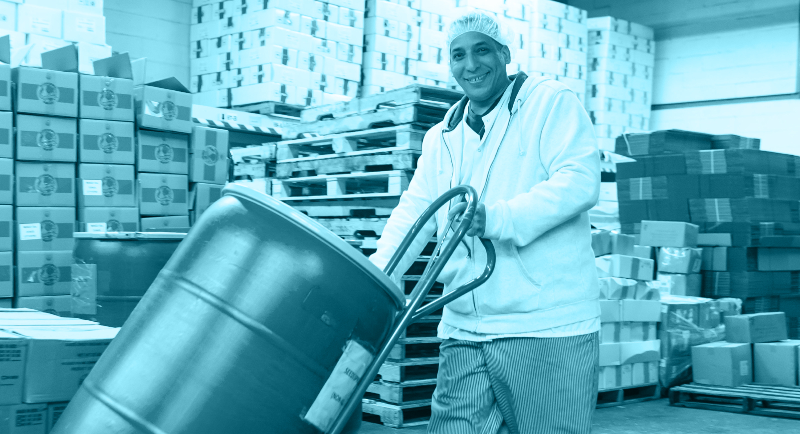 Man in a hair net transporting a barrel of food across a warehouse floor