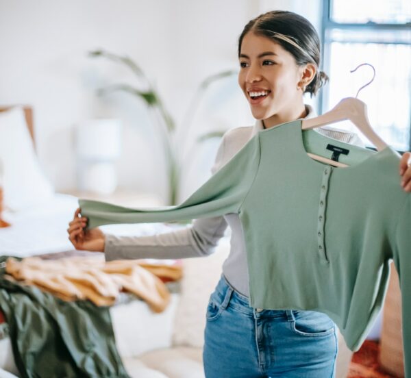 Woman holding up green top on hanger and smiling.
