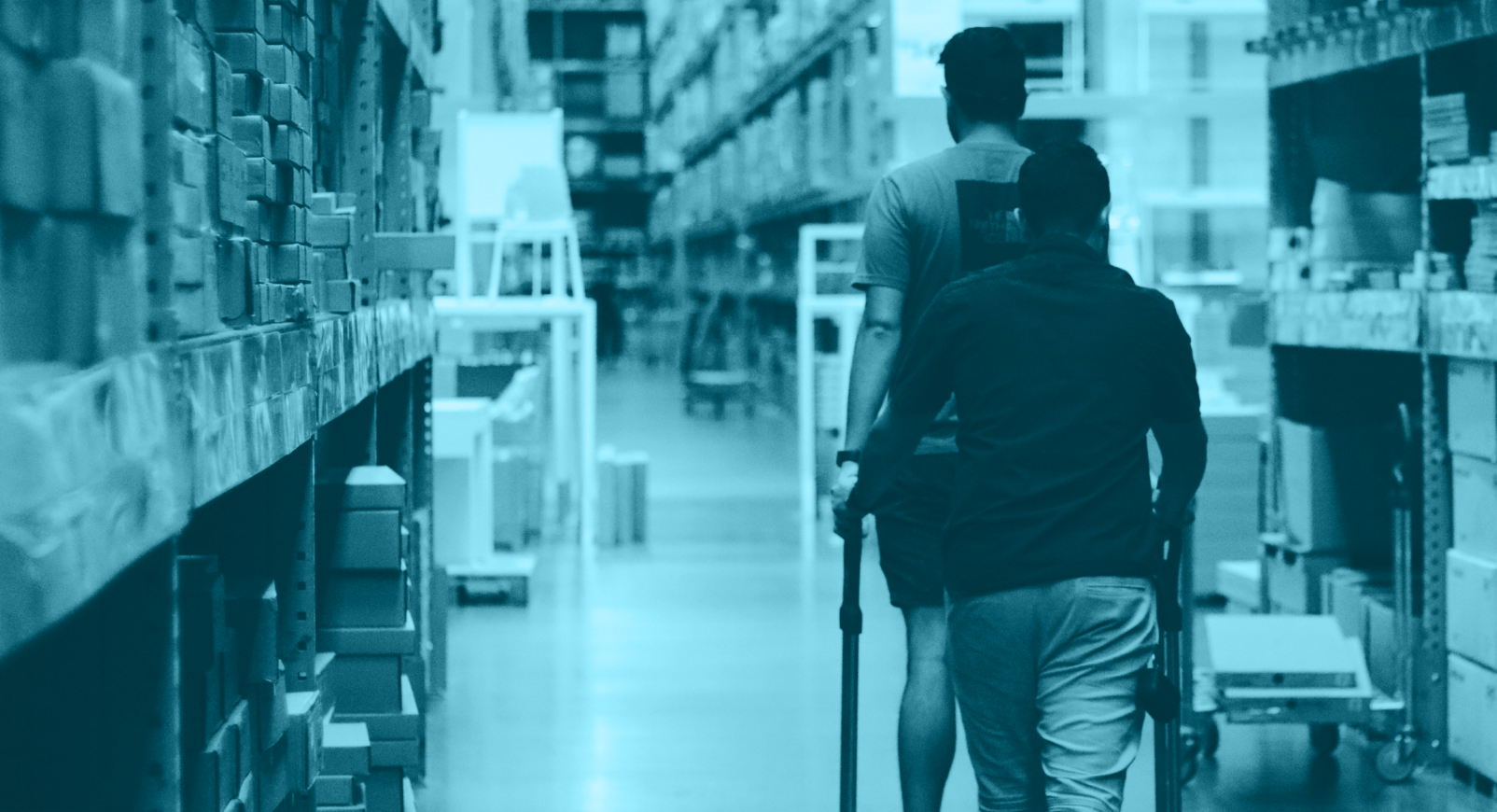 Two people walking between stacked shelves in a warehouse