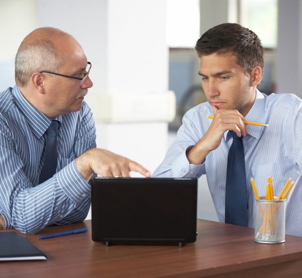 Senior and junior businessman discussing in front of a laptop