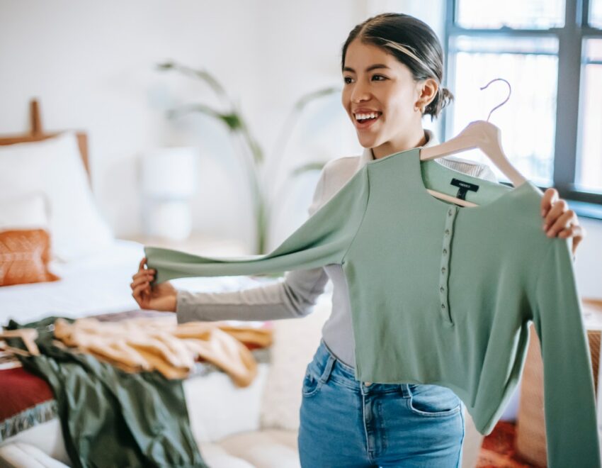 Woman holding up green top on hanger and smiling.