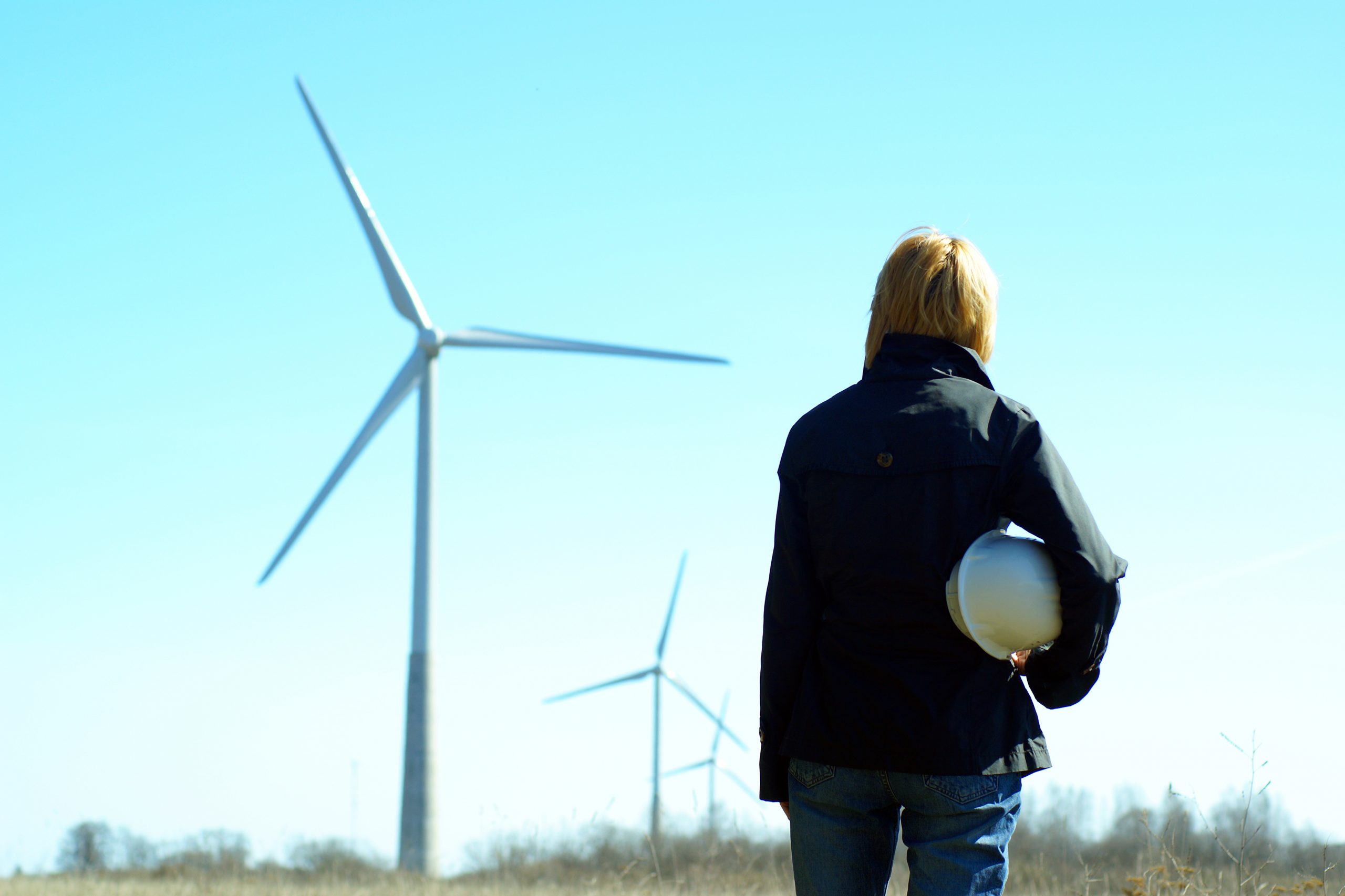 Woman engineer stood in front of a wind turbines