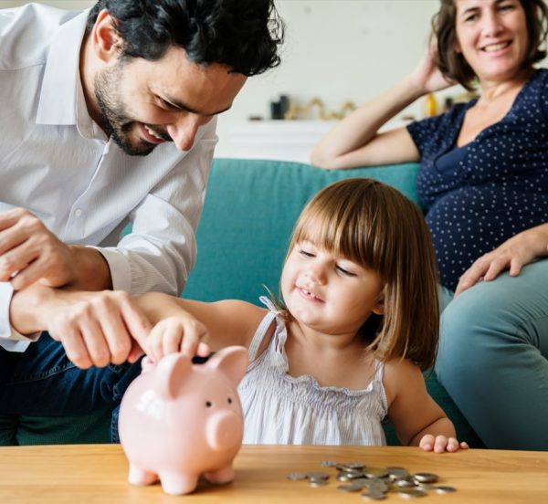 Man and woman with child putting money in to a piggy bank. Links to Help with childcare costs and other support for families