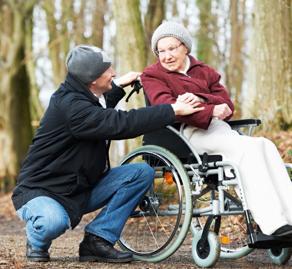 Man supporting an older woman who is in a wheel chair